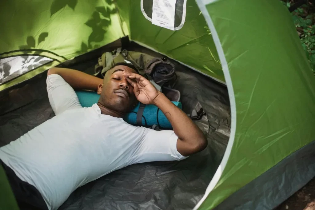 African American male traveler with closed eyes resting in tent and rubbing eyes during nap