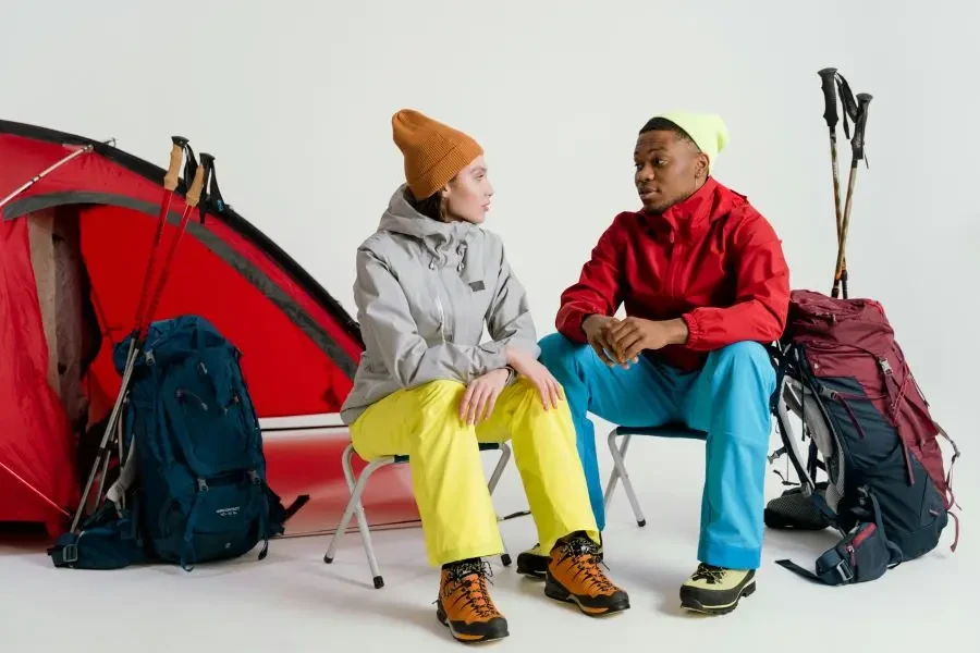 Two campers sit with hiking gear and tent in a studio setting