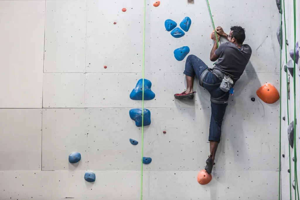 A Man Scales The Side Of A Rock Climbing Wall