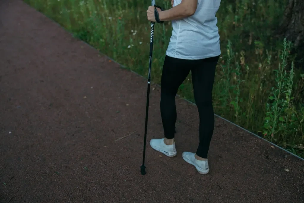 A person in athletic wear uses a trekking pole while walking on a forest pathway