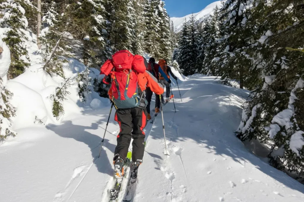 Group of skiers in winter gear traversing a snowy mountain trail surrounded