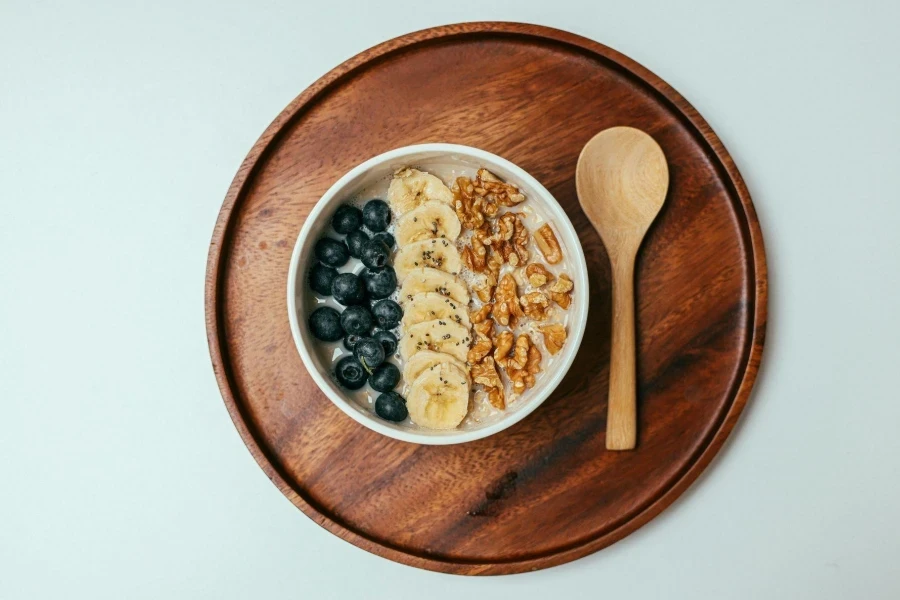 A Bowl of Oatmeal Beside a Wooden Spoon on a Wooden Tray