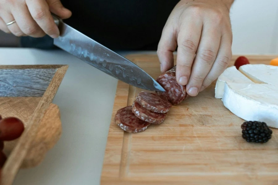 A Person Slicing Salami on a Wooden Chopping Board