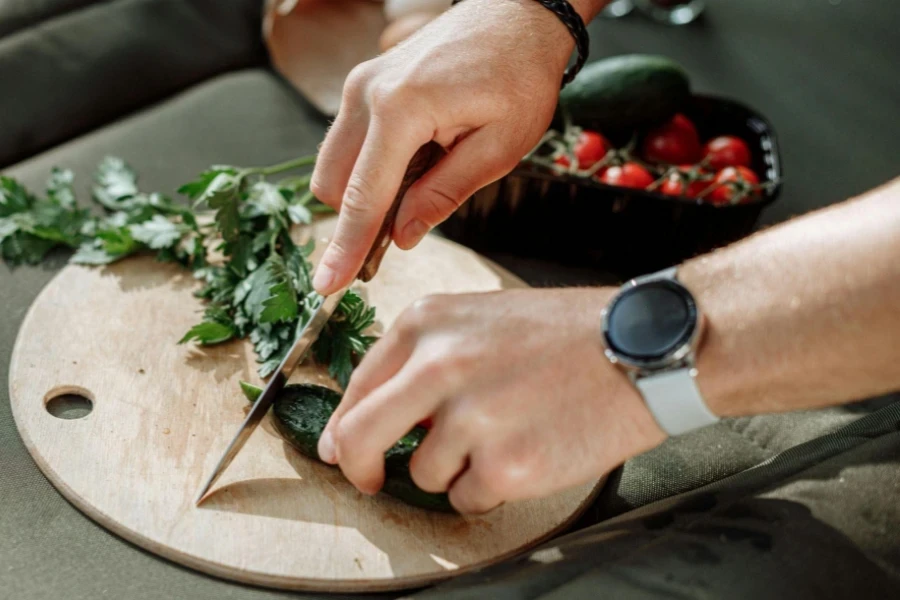 A Person Slicing the Cucumber on a Wooden Chopping Board