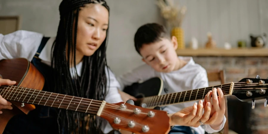 A Woman Teaching a Boy How to Play a Guitar