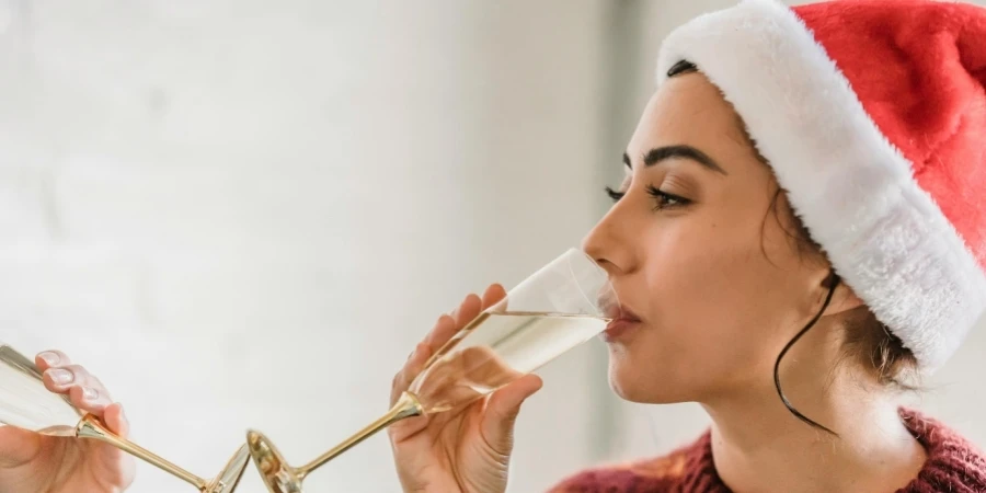 A person wearing a santa hat drinking from a glass