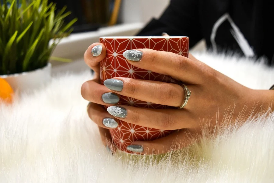 A person with chrome nails holding a mug