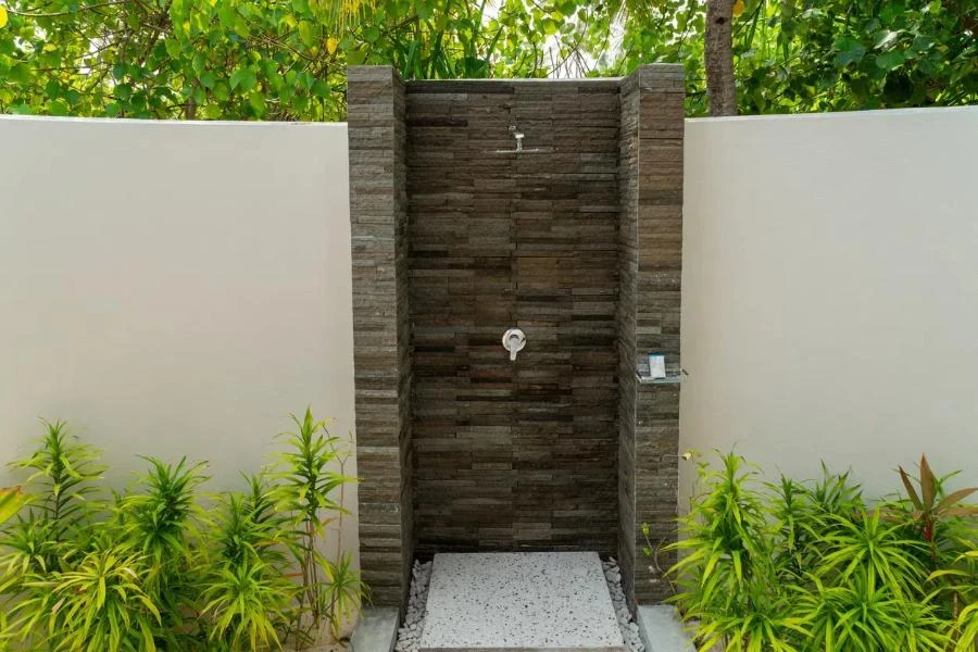 A wall-mounted outdoor shower surrounded by plants