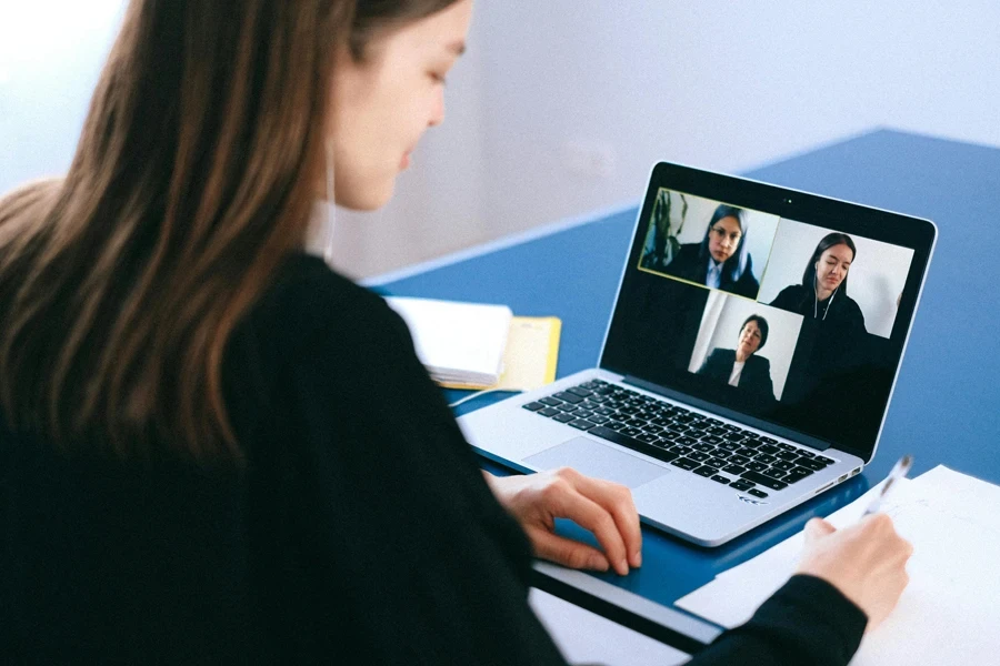 A woman engaging in a video conference using a laptop at home, taking notes