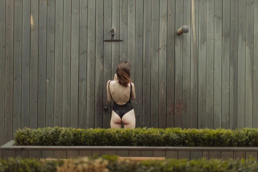 A woman using outdoor shower mounted on a wall