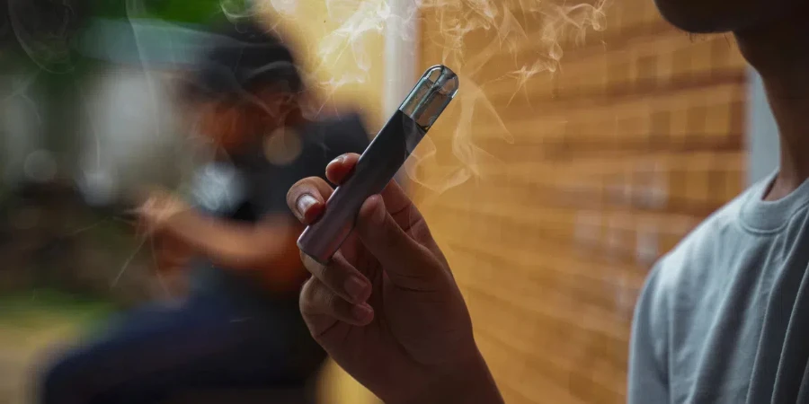 Asian male teenager holds a smoked e-cigarette