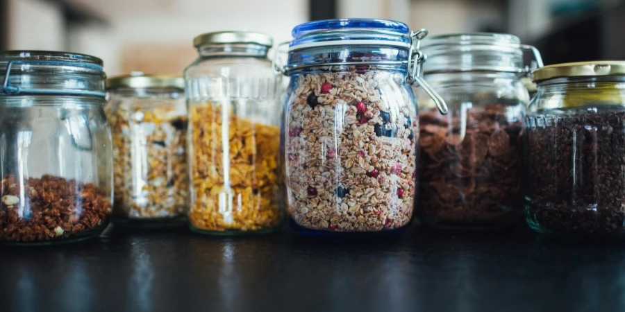 Close-up of various cereals in glass jars on a kitchen counter, showcasing diverse breakfast options