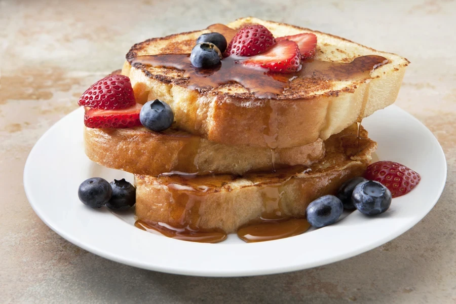 French toast with fruit and syrup on a marble countertop