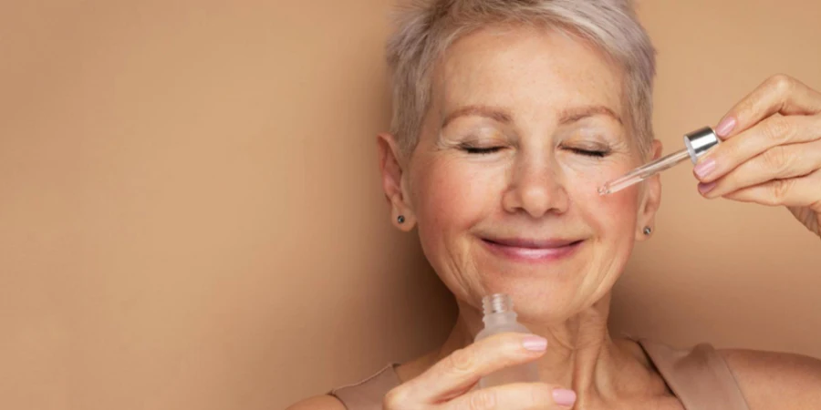 Happy Senior Lady Applies Cosmetic Oil Serum on Face