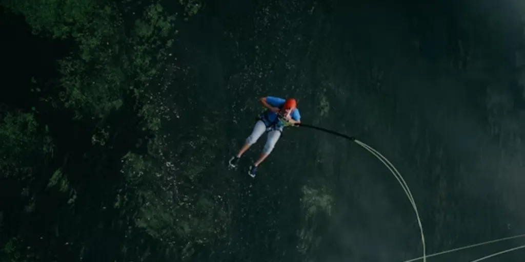 Man attached to bungee jumping cords jumping over water