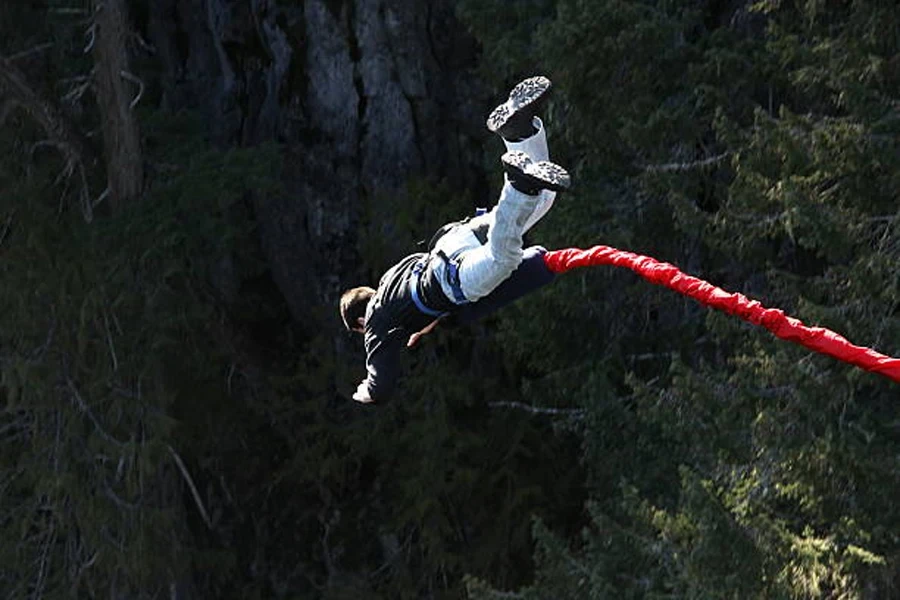 Man attached to red bungee cord jumping into void