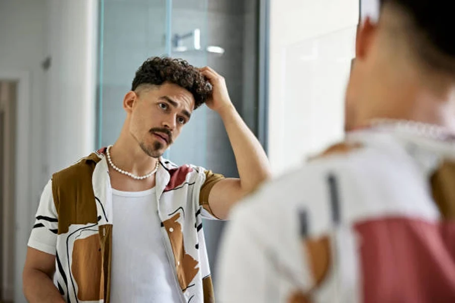 Man holding hair while looking in bathroom mirror