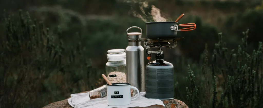 Peralatan memasak berkemah di luar ruangan dengan kompor, panci, dan cangkir di atas batu di alam