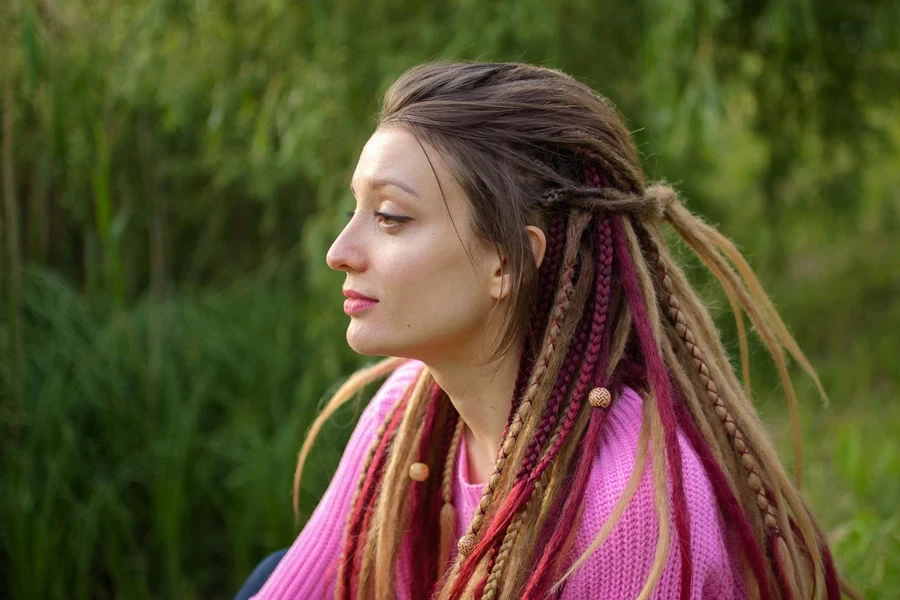 Outdoors Female Portrait of a Modern Girl with Dreadlocks Wearing Pink Sweater and Dark Jeans in a City Park