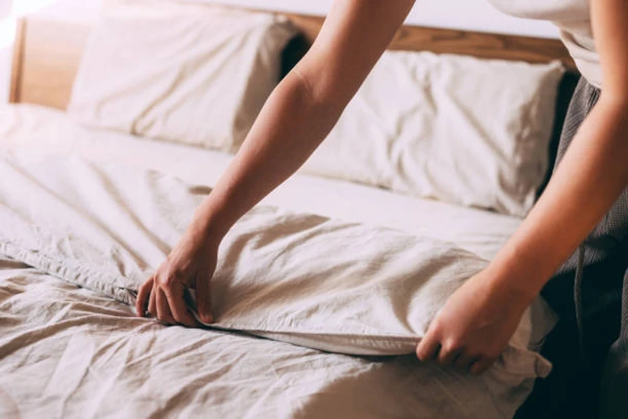 Person Making Bed with Fresh White Sheets at Home