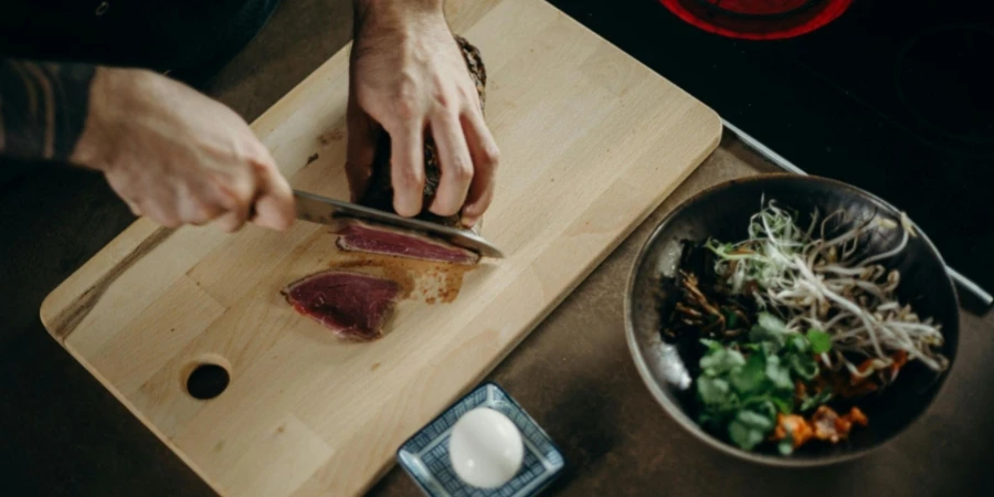 Person Slicing Meat on Wooden Chopping Board