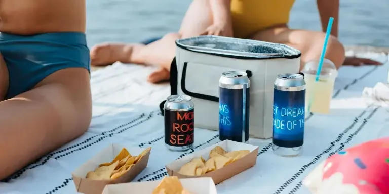 Relaxing summer picnic by the water with snacks, drinks, and swimwear