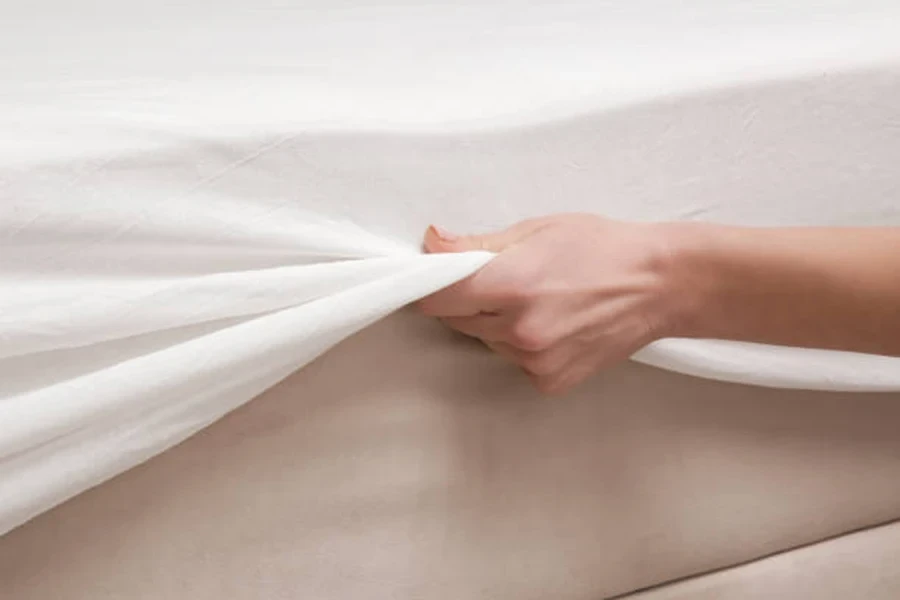 Woman Is Putting on a Fitted White Cotton Sheet on a Mattress While Making the Bed