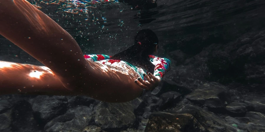 Woman Swimming Underwater Above Rocks