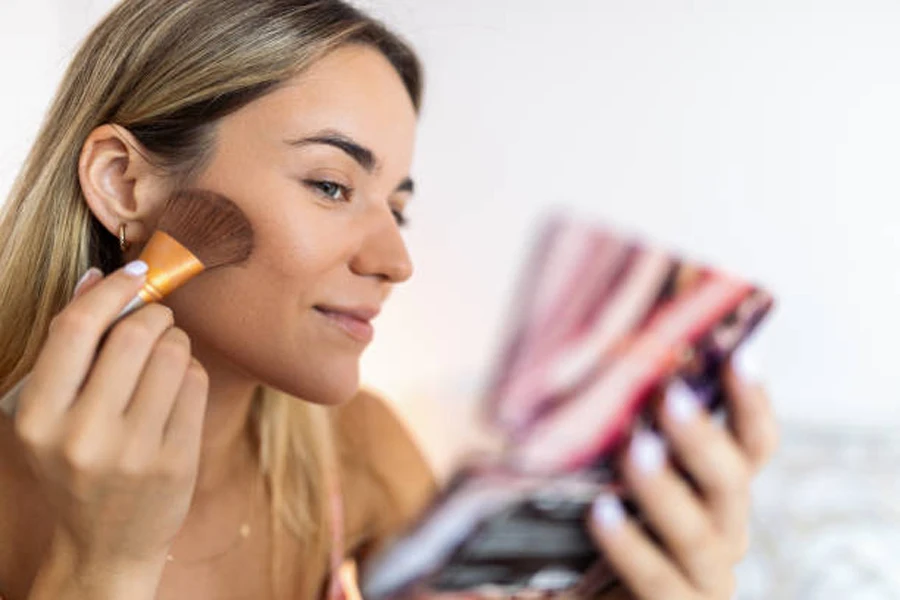 Woman applying blush to cheeks while holding mirror