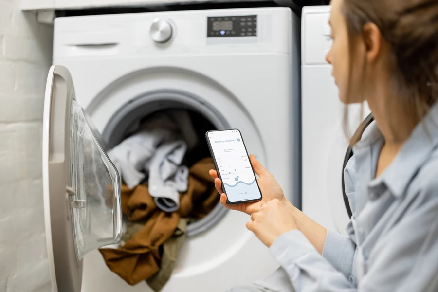 Woman controlling washing machine with a smartphone