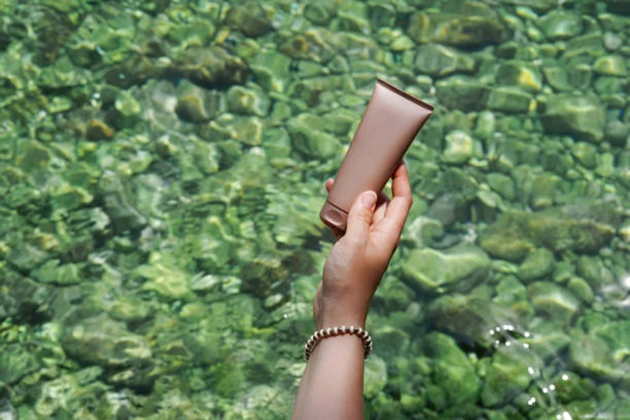 Woman holding tube of hand lotion at body of water