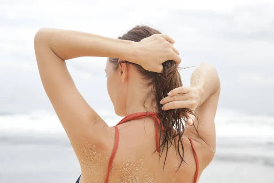 Woman using hair care product at beach with wet hair