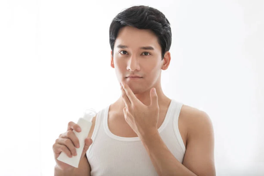 Young man applying cream to face with no acne