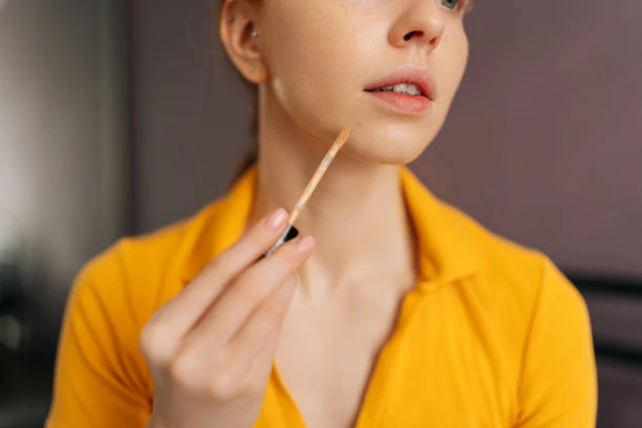 Young woman applying liquid concealer to chin area