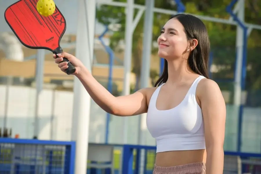 Young woman playing pickleball outdoors wearing sportswear, enjoying a sunny day