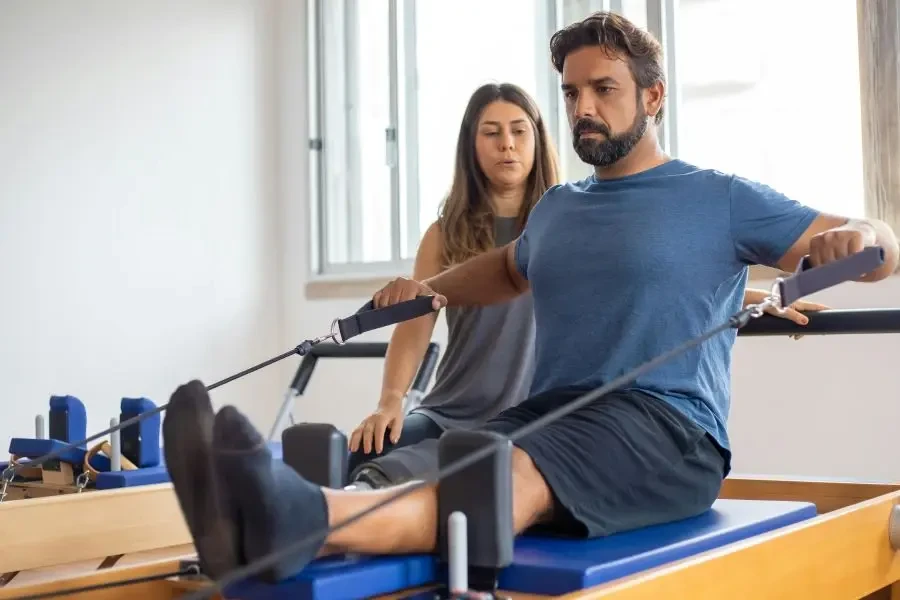 Man with prosthetic leg working out with trainer in gym, showcasing strength and rehabilitation