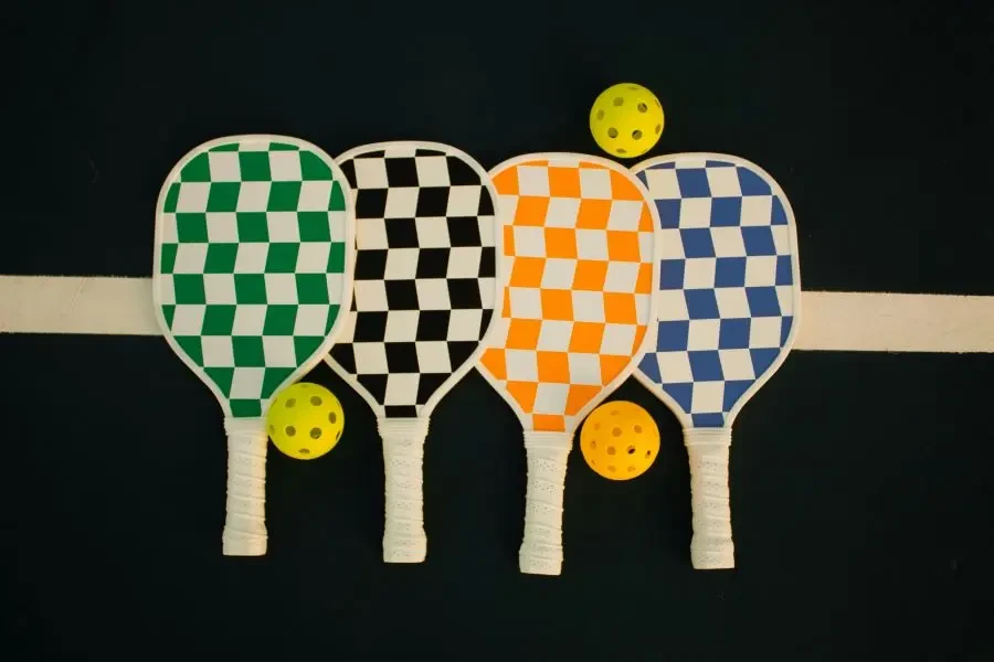 Four checkerboard-patterned pickleball paddles with wiffle balls on a sports court