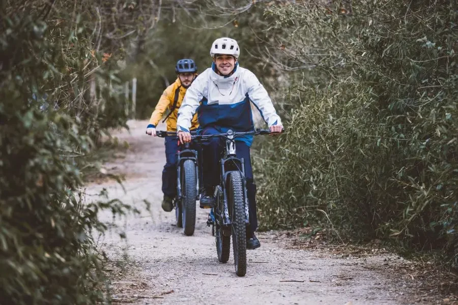 Two men ride bicycles along a forest path, enjoying a day of recreation outdoors