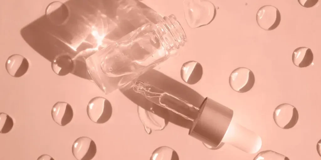 A bottle of cosmetic product with bubbles casts a shadow on a beige background with gel drops