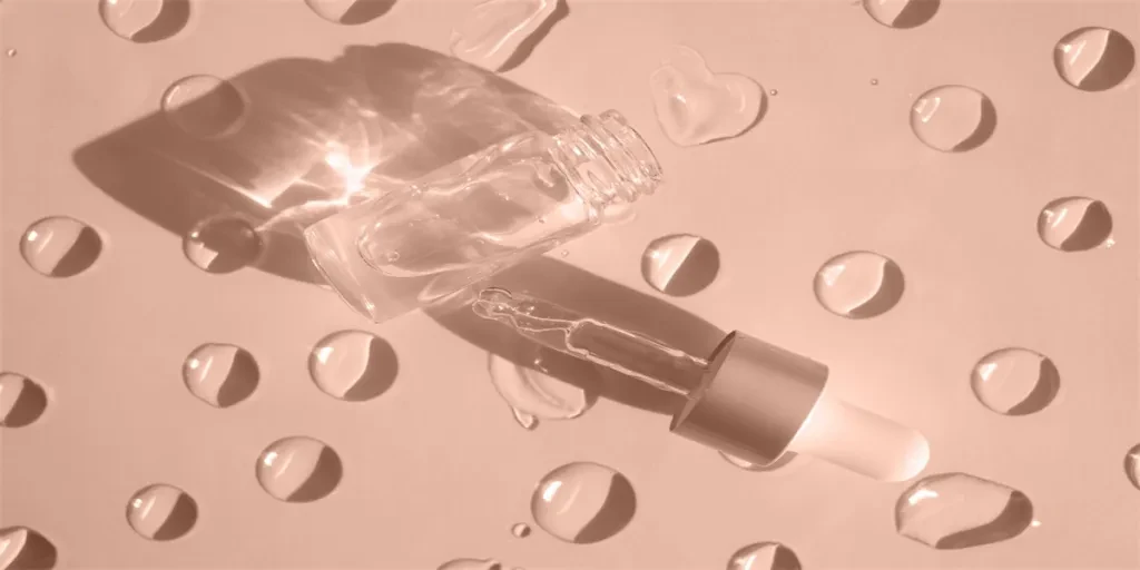 A bottle of cosmetic product with bubbles casts a shadow on a beige background with gel drops