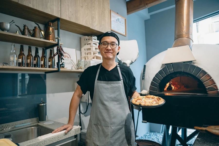 A chef with pizza in front of a wood-fired oven