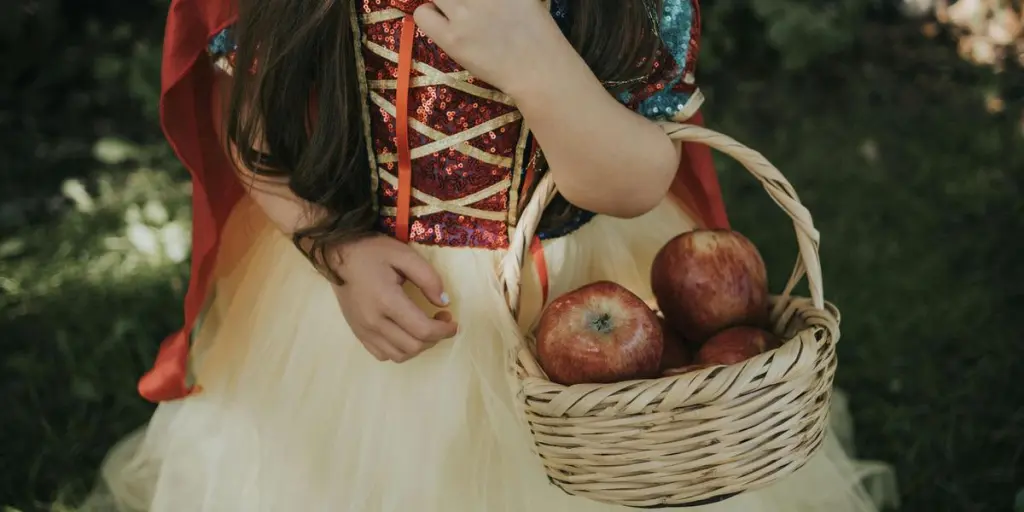 A child in a fairy tale costume holding a basket of apples while standing outdoors