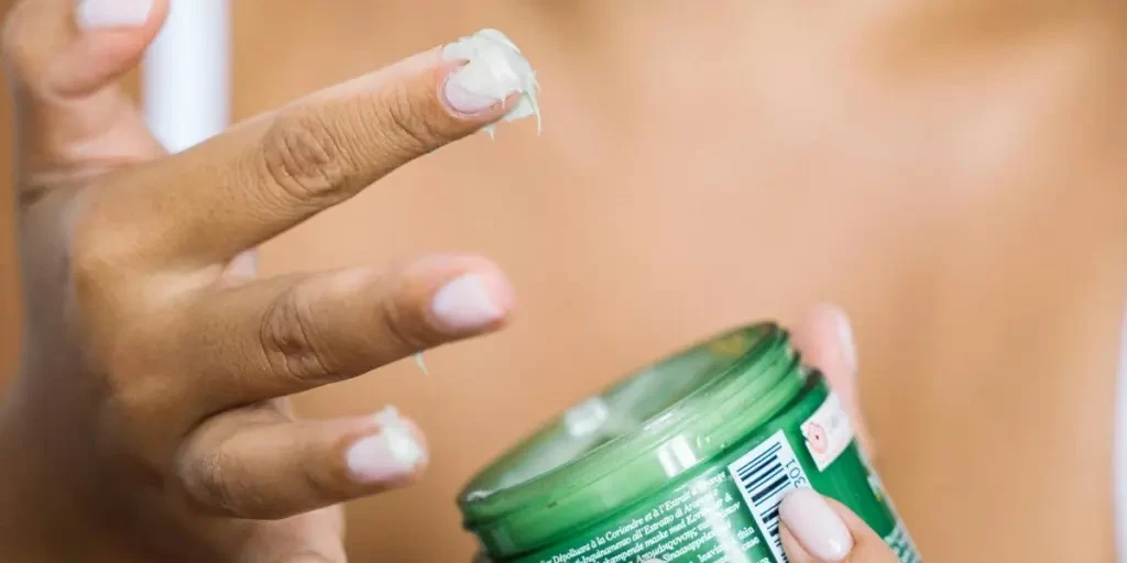 A close-up of a woman applying skincare cream with focus on hands and product