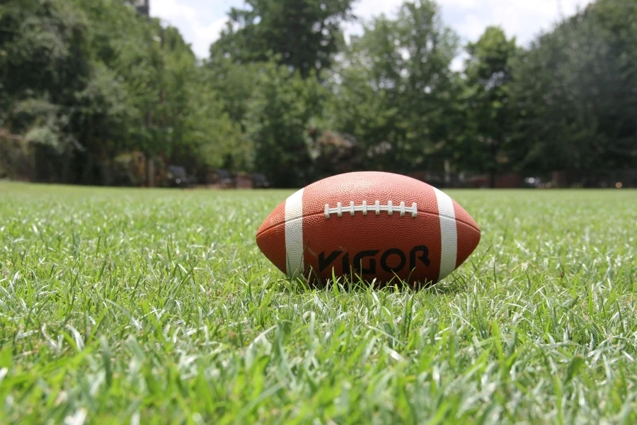 A close-up of an American football on a grassy field, highlighting outdoor sports in summer