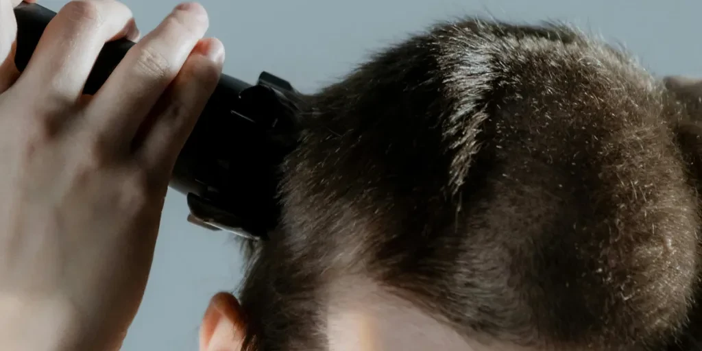 A close-up portrait of a woman using an electric razor to shave her head by cottonbro studio