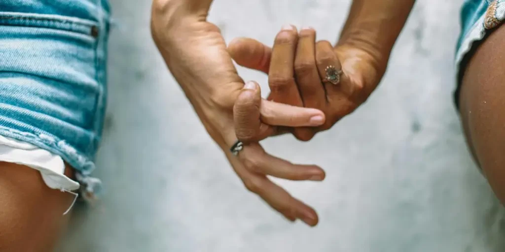 A close-up shot of two people holding hands, wearing rings and denim shorts, symbolizing connection