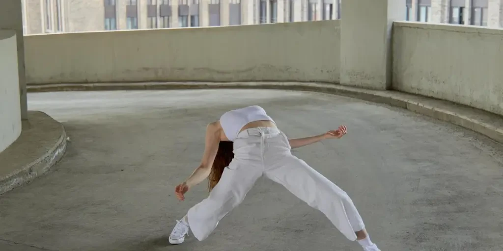 A dancer in a creative pose wearing white attire in an urban parking deck