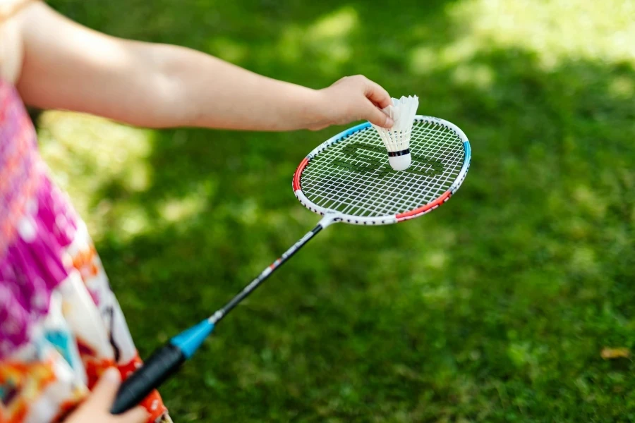 A detailed close-up of a person holding a badminton racket and shuttlecock outdoors by Photo