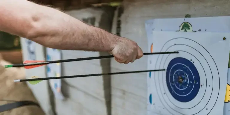 A focused arm holding arrows near a target in an archery practice setting
