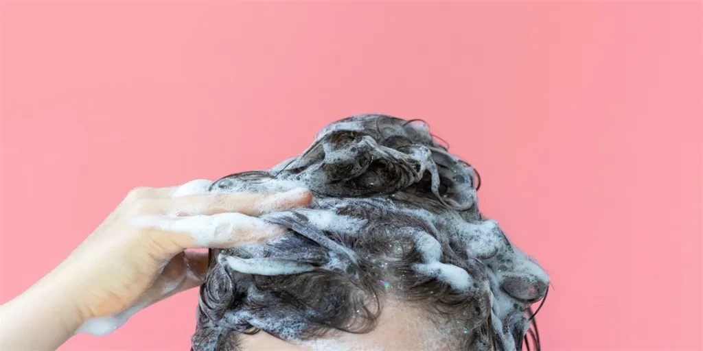 A girl washes her hair with shampoo on a pink background